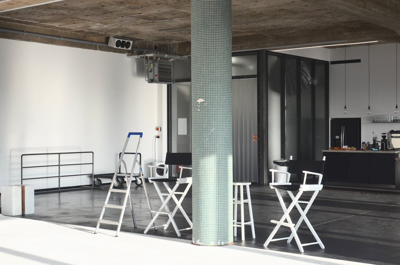 Interior of spacious studio with stools near column and kitchen counter with kitchenware placed in contemporary room with bright sunlight